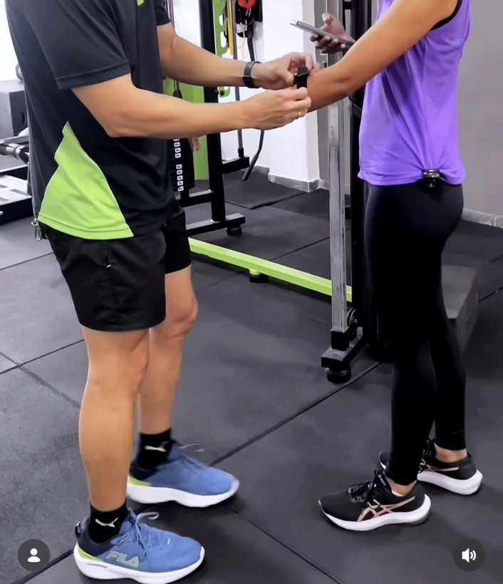 Personal ajustando uma pulseira inteligente Moovz no braço de uma aluna